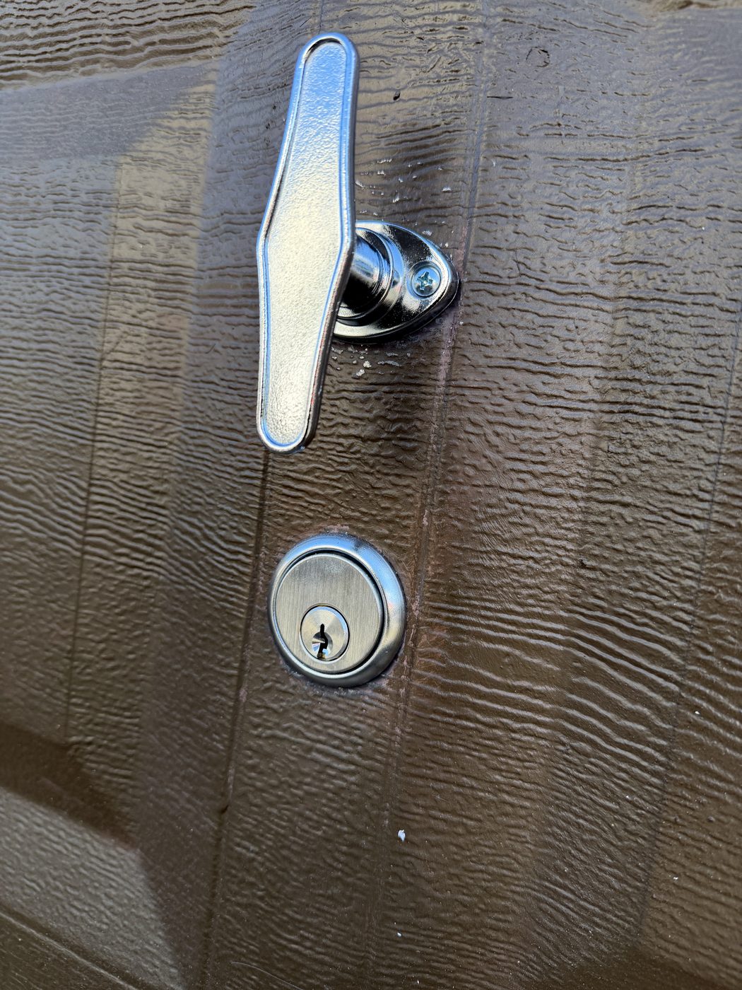 A T-handle and keyed cylinder on a garage door — the lock on the door itself, not the opener